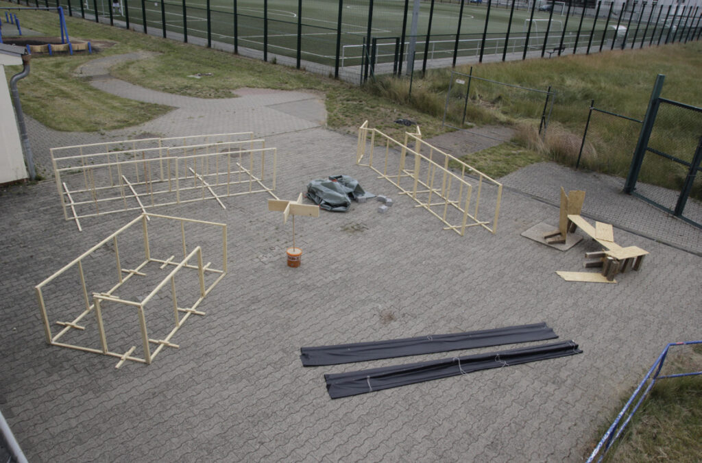 Das Bild zeigt alle sechs Skulpturen "Umstände" in Vogelperspektive, auf einen gepflasterten Platz aufgestellt, mit grünen Wiesen un einem Sportplatz drum herum.