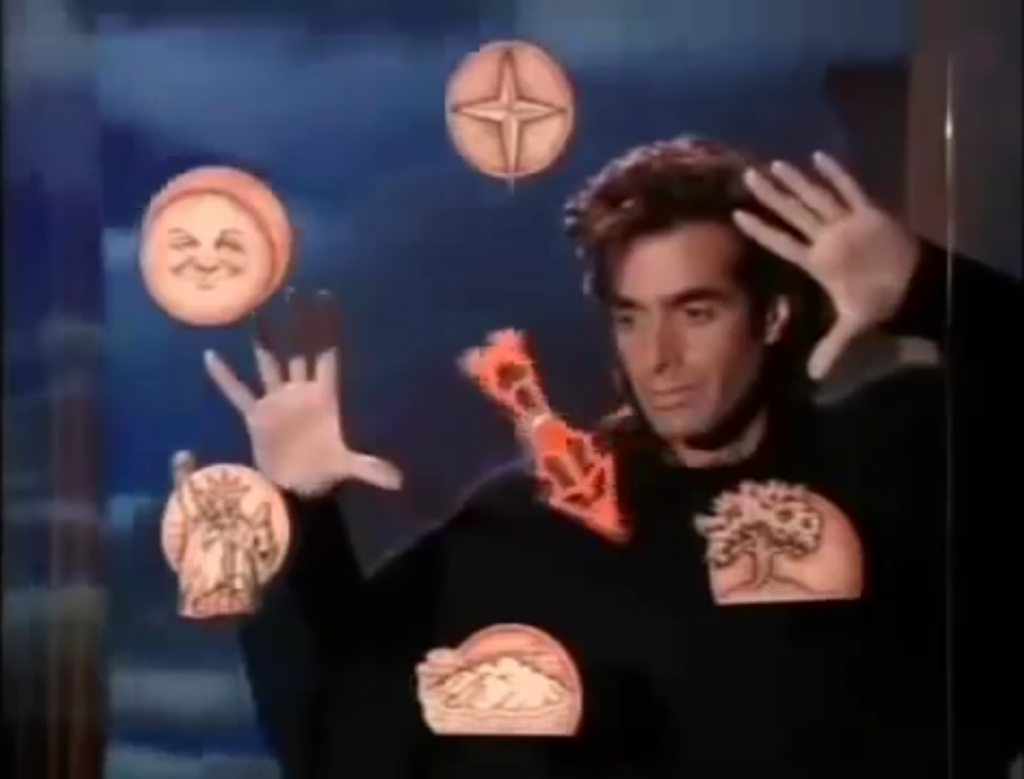 Das Bild zeigt einen Filmstill von "Sweaty Transition" mit blauen, beigen und schwarzen Farbtönen. Es zeigt einen berühmten Zauberkünstler David Copperfield der vor einer Glasscheibe, mit erhobenen Armen steht. Auf der Glasscheibe sind runde, beige Symbole und ein roter Pfeil. Seine Augen schauen auf den Pfeil. Hinter den Zauberkünstler ist ein blauer Himmel.